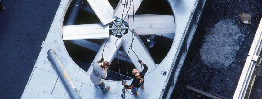 central-plant Two workers prepare to repair an industrial fan on the roof of a multistory building.