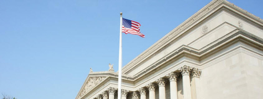 Daytime exterior of a corner of the National Archives building in Washington, D.C. with the United States Flag flying in front