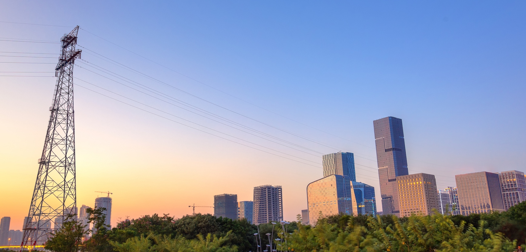 View of a city at dusk with a high-tension tower and power lines in the foreground