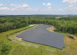 Daytime aerial view of a Blue Cross Blue Shield of Massachusetts solar farm in a wooded area