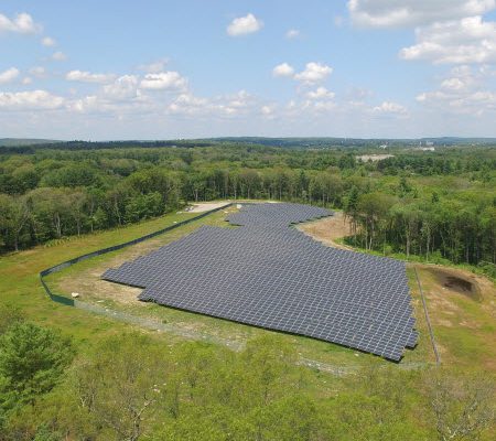 Daytime aerial view of a Blue Cross Blue Shield of Massachusetts solar farm in a wooded area