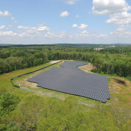 blue-cross-blue-shield-featured-image Daytime aerial view of a Blue Cross Blue Shield of Massachusetts solar farm in a wooded area