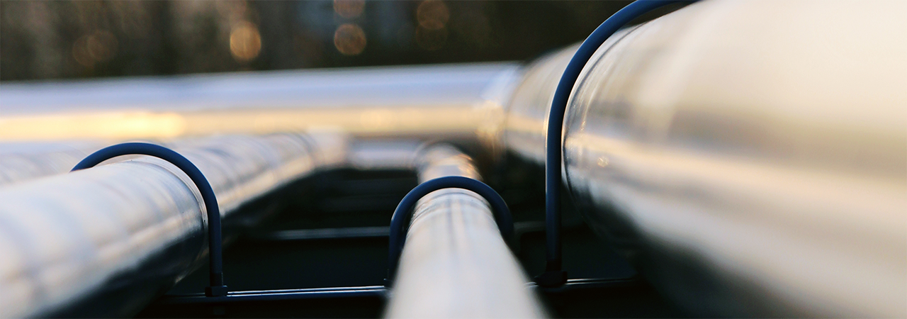 Daytime closeup of pipes that stretch back toward an energy plant in the distance