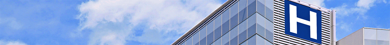 Daytime exterior view of the top of a hospital building with a large, blue H mounted on the side.