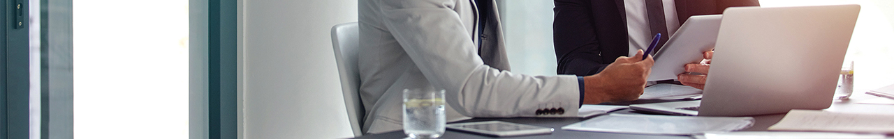 Daytime interior view shows a worker in an office handing a pen to a person holding a tablet computer