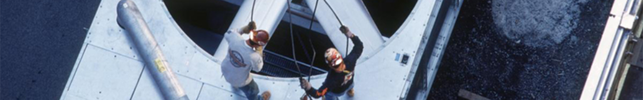 Daytime aerial view of two workers repairing a large fan on top of a building