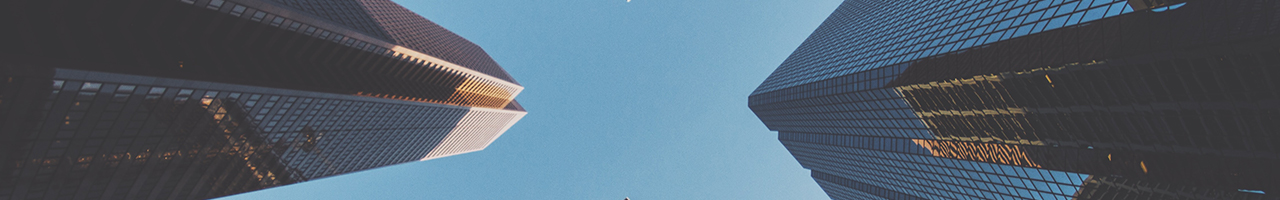 Daytime view looking up at two skyscrapers, one brown and one black, beneath a clear, blue sky