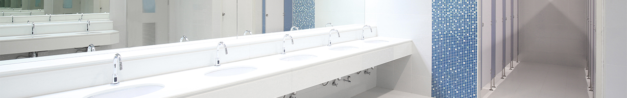 Interior view of a modern bathroom in a large building shows a row of faucets with hands-free sensors