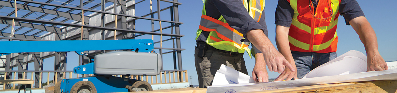 Daytime closeup of two workers reviewing blueprints at a construction site