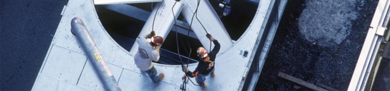 Daytime overhead view of workers servicing a large fan system on the roof of a building