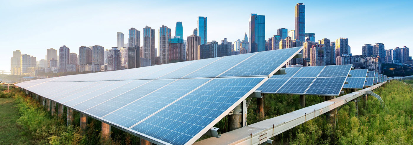 Daytime closeup of solar panels in a solar farm with a city skyline in the bacckground