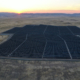 Aerial view of a solar farm in San Joaquin County with the sun setting behind mountains in the distance