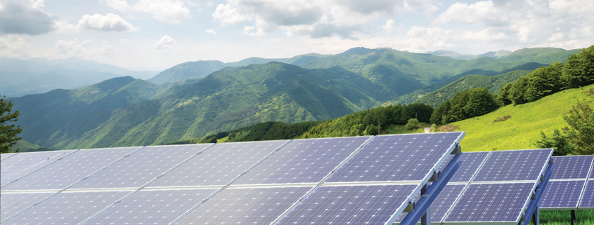 Daytime view of solar panels with mountains in background and blue sky