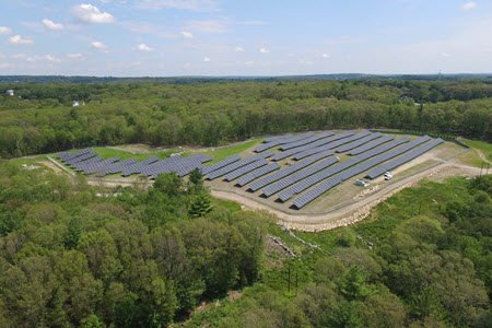 Daytime aerial view of a solar farm in a wooded area