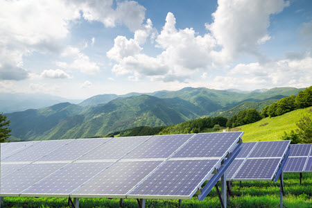 Daytime view of solar panels mounted in arrays on a hillside with mountains in the background