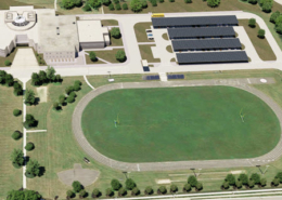 Aerial view of John Paiul II Catholic Secondary School in Ontario, Canada with rendered solar car ports and battery storage systems