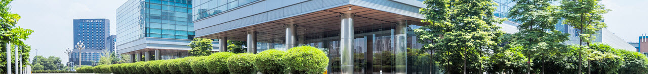 Daytime view of a commercial park showing glass buildings surrounded by trees and shrubs