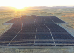 Aerial view of a large solar farm in San Joaquin County with the sun setting behind mountains in the distance