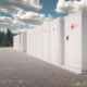Daytime view of large-scale battery storage enclosures with an evergreen forest in the background