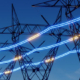 Grid modernization concept image shows a row of high-tension electrical towers connected by blue and yellow lines of light