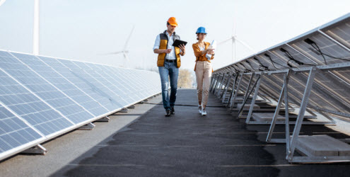 Daytime view of a man and a woman in hard hats inspecting a rooftop solar array